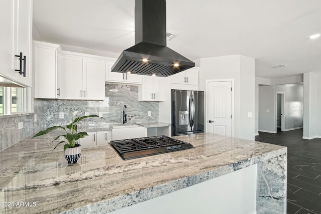 kitchen featuring stainless steel fridge, island range hood, light stone countertops, white cabinetry, and a sink