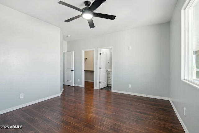 unfurnished bedroom featuring a ceiling fan, a walk in closet, baseboards, and wood finished floors