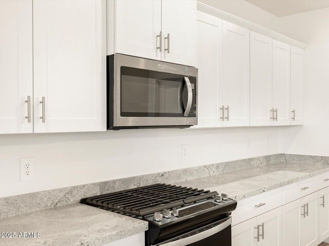 kitchen with white cabinets, light stone countertops, and gas range oven