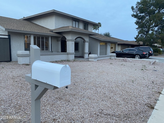 view of front facade with stucco siding, roof with shingles, and driveway