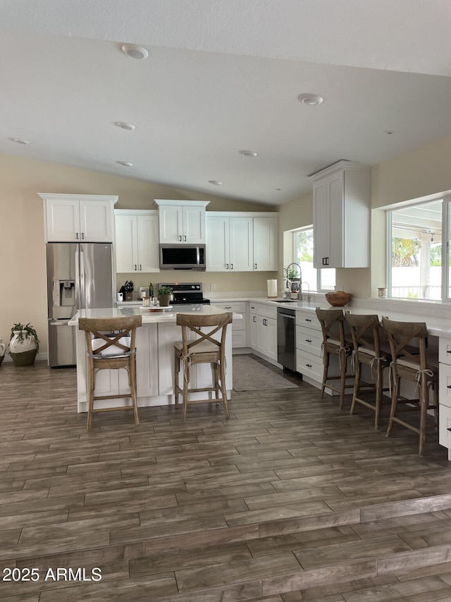 kitchen with white cabinetry, appliances with stainless steel finishes, a breakfast bar area, lofted ceiling, and dark wood-style flooring