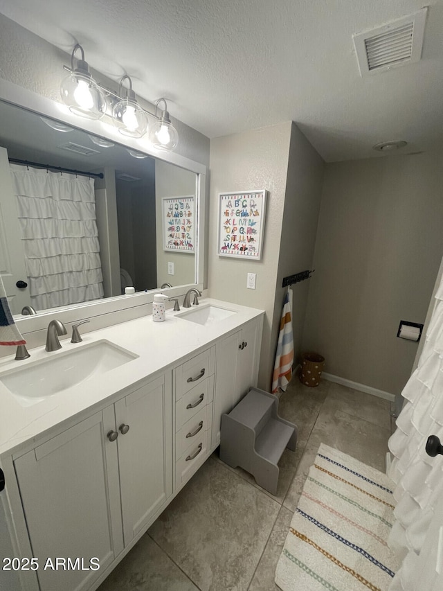 full bath featuring double vanity, visible vents, a textured ceiling, and a sink