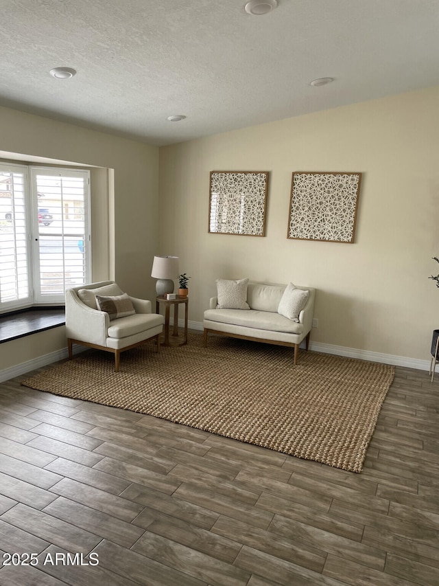 living area featuring a textured ceiling, baseboards, and wood finish floors