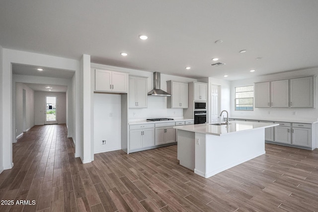 kitchen featuring black appliances, wall chimney exhaust hood, dark hardwood / wood-style flooring, sink, and a kitchen island with sink