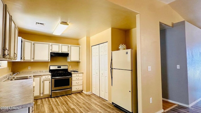 kitchen featuring freestanding refrigerator, stainless steel gas range oven, under cabinet range hood, a sink, and light wood finished floors