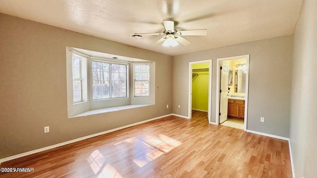 unfurnished bedroom with light wood finished floors, a walk in closet, baseboards, and a closet