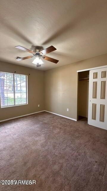 unfurnished bedroom with dark carpet, baseboards, a closet, and a ceiling fan