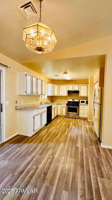 kitchen featuring stainless steel gas range oven, freestanding refrigerator, dishwasher, light wood-type flooring, and a chandelier