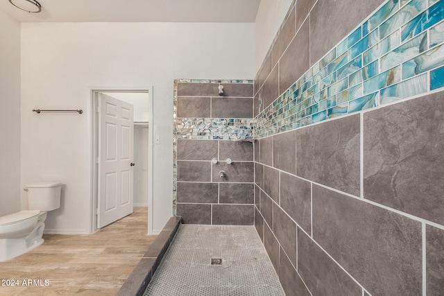 bathroom with a tile shower, toilet, and hardwood / wood-style floors