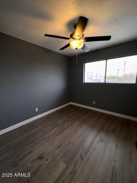 empty room with a textured ceiling, dark wood finished floors, a ceiling fan, and baseboards