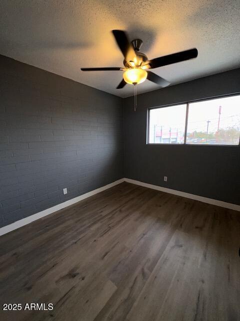 unfurnished room with dark wood-type flooring, a textured ceiling, baseboards, and a ceiling fan