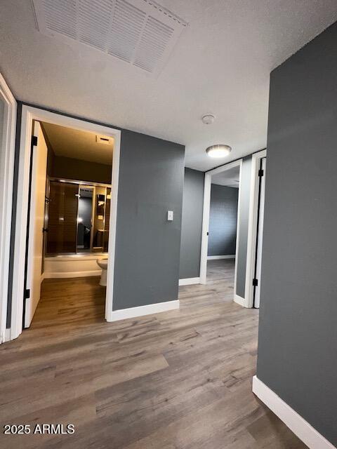 hall featuring baseboards, visible vents, and wood finished floors