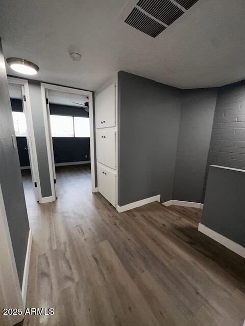 hallway with a textured ceiling, wood finished floors, visible vents, and baseboards