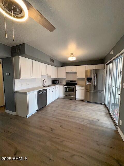 kitchen with appliances with stainless steel finishes, white cabinets, a sink, a textured ceiling, and wood finished floors