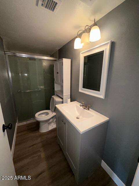 bathroom featuring toilet, wood finished floors, vanity, visible vents, and a stall shower