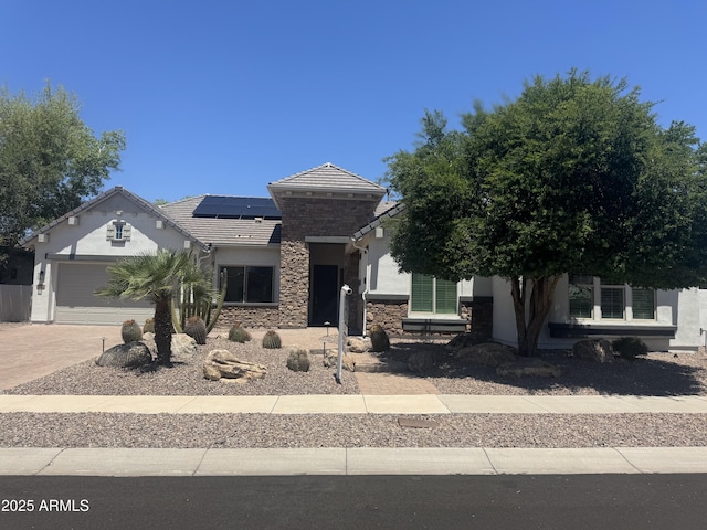 view of front of home featuring stone siding, stucco siding, a tiled roof, roof mounted solar panels, and driveway