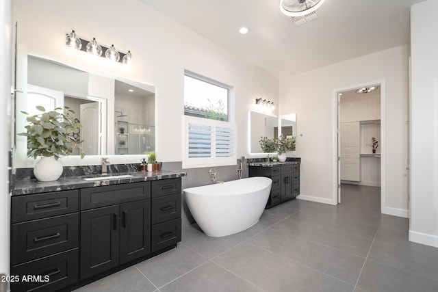 bathroom with a shower stall, tile patterned flooring, two vanities, a soaking tub, and baseboards