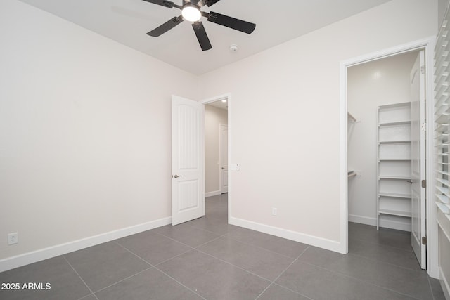 unfurnished bedroom featuring a walk in closet, dark tile patterned floors, baseboards, and a ceiling fan
