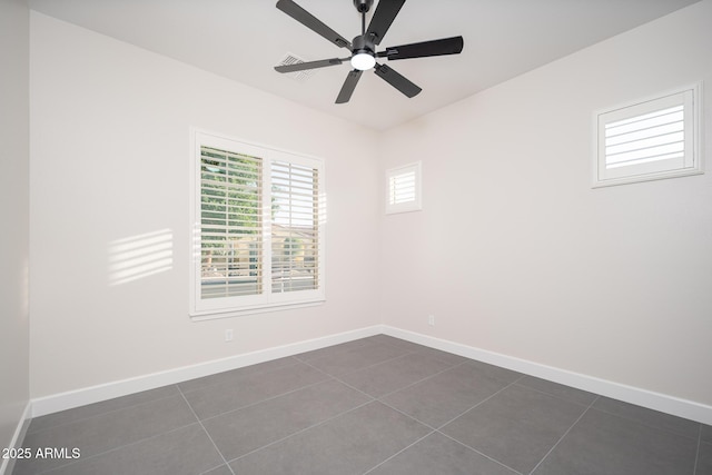 empty room with a ceiling fan, dark tile patterned flooring, and baseboards