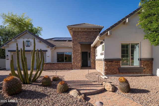 view of front of home featuring stone siding, stucco siding, and roof mounted solar panels