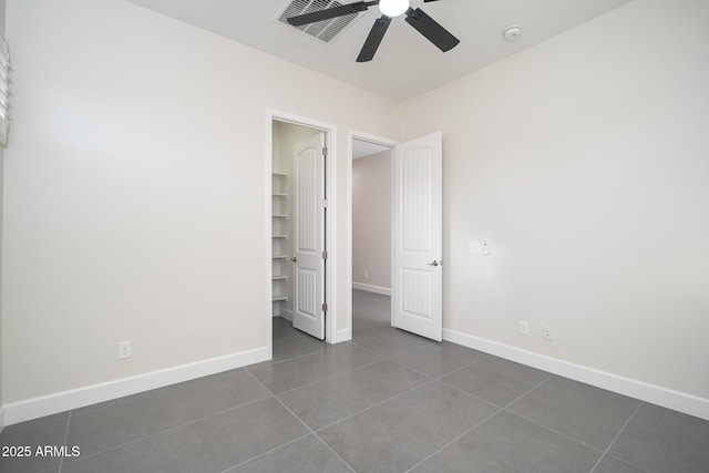 unfurnished bedroom with dark tile patterned floors, a walk in closet, baseboards, and a ceiling fan