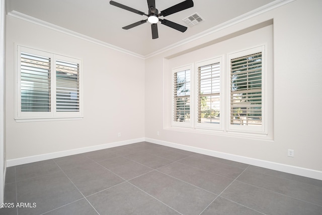 unfurnished room with ornamental molding, healthy amount of natural light, a ceiling fan, dark tile patterned flooring, and baseboards