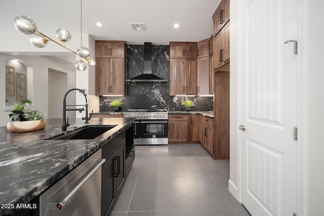 kitchen with wall chimney range hood, appliances with stainless steel finishes, a sink, brown cabinetry, and backsplash
