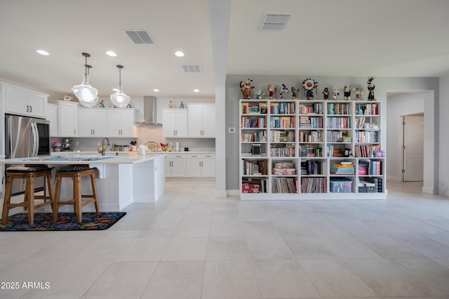 kitchen with pendant lighting, an island with sink, white cabinets, a kitchen bar, and wall chimney range hood