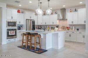 kitchen with white cabinetry, wall chimney exhaust hood, stainless steel appliances, and a center island with sink