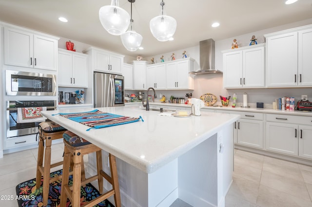 kitchen with pendant lighting, wall chimney range hood, stainless steel appliances, and white cabinets