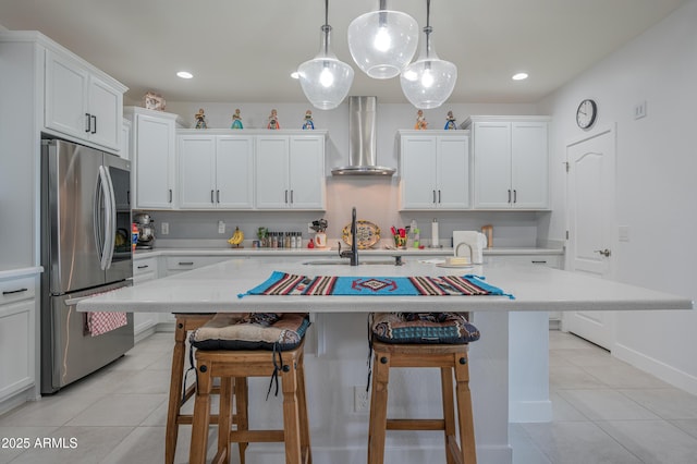 kitchen with stainless steel refrigerator, wall chimney exhaust hood, a center island with sink, and pendant lighting