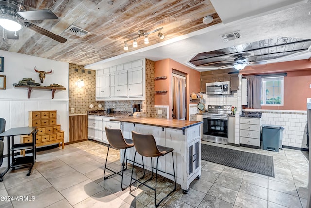 kitchen with white cabinets, a breakfast bar area, tasteful backsplash, butcher block countertops, and appliances with stainless steel finishes