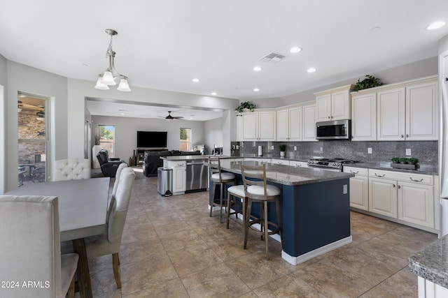 kitchen featuring hanging light fixtures, ceiling fan, dark stone countertops, appliances with stainless steel finishes, and a breakfast bar area