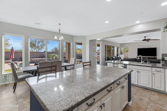 kitchen with pendant lighting, white cabinets, ceiling fan with notable chandelier, light stone countertops, and a kitchen island