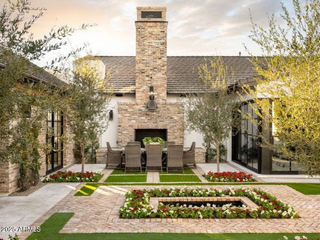 back house at dusk with an outdoor brick fireplace and a patio area