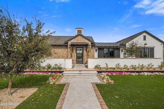 exterior space with a front yard, a standing seam roof, brick siding, and metal roof