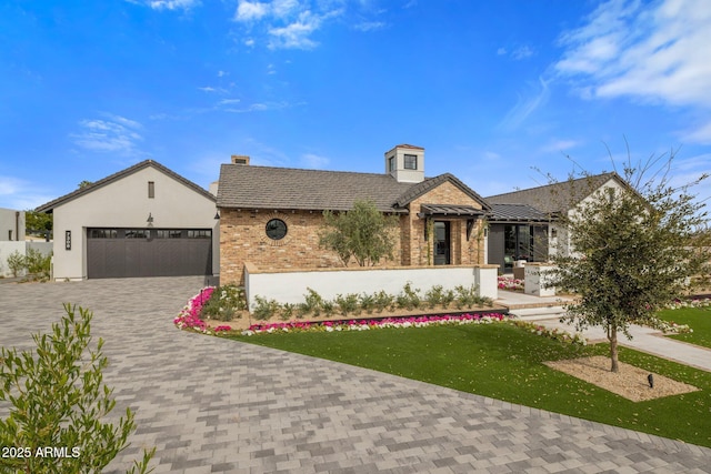 view of front of property with an attached garage, a chimney, decorative driveway, and brick siding