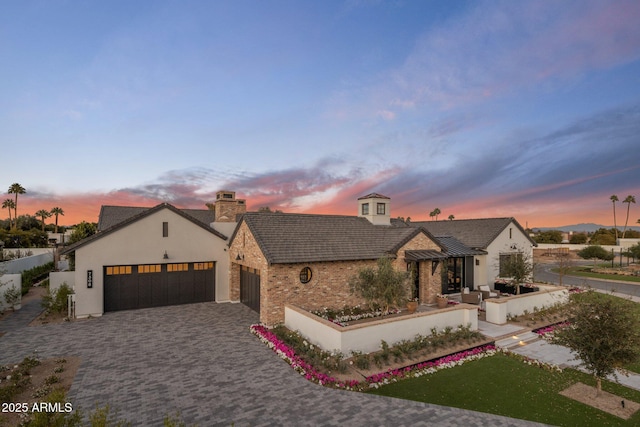 view of front of home featuring decorative driveway, a chimney, a standing seam roof, metal roof, and a garage