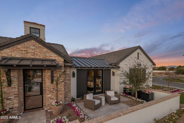 back of property at dusk with a patio area, a standing seam roof, brick siding, and metal roof