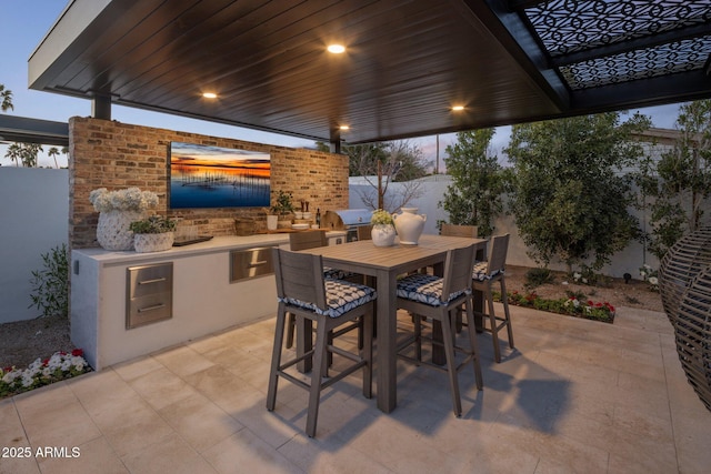 patio terrace at dusk with outdoor dining area, fence, grilling area, and area for grilling