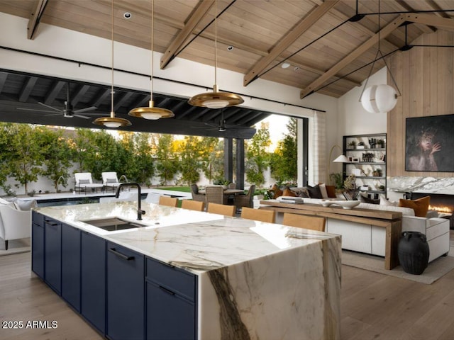 kitchen featuring pendant lighting, beam ceiling, a center island with sink, open floor plan, and a sink