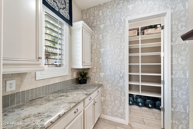 interior space with tasteful backsplash, light stone counters, and white cabinets