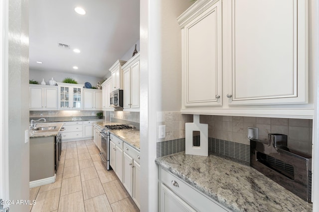 kitchen featuring decorative backsplash, light stone counters, stainless steel appliances, sink, and white cabinetry