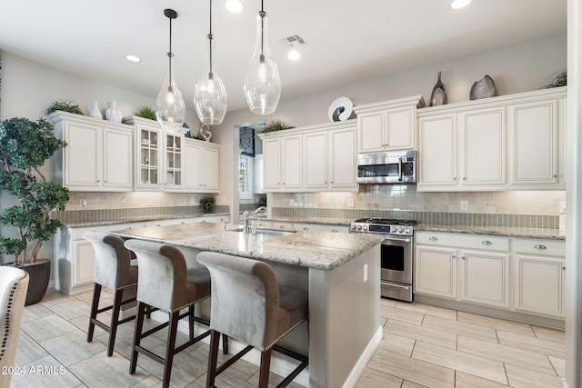 kitchen with sink, light stone counters, an island with sink, a breakfast bar area, and appliances with stainless steel finishes