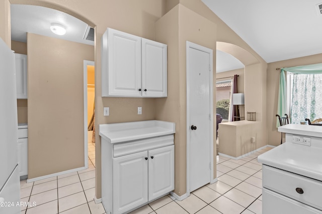 kitchen featuring white cabinets, light tile patterned floors, and vaulted ceiling