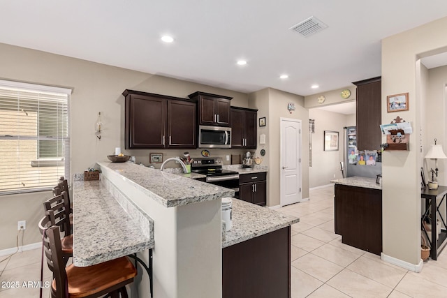 kitchen featuring light tile patterned floors, a breakfast bar, appliances with stainless steel finishes, light stone counters, and kitchen peninsula