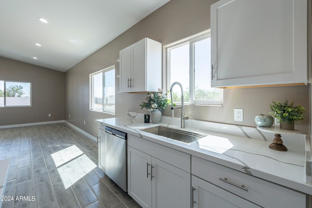 kitchen with dishwasher, white cabinets, sink, vaulted ceiling, and light stone countertops