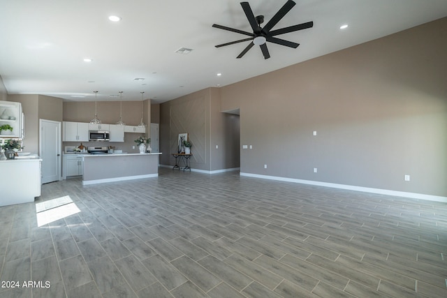 unfurnished living room with ceiling fan and a high ceiling