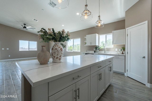 kitchen featuring a kitchen island, light stone counters, white cabinetry, and hanging light fixtures