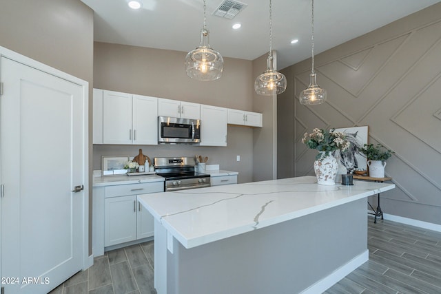 kitchen with white cabinetry, stainless steel appliances, light stone counters, decorative light fixtures, and a kitchen island